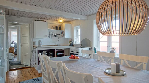 Een moderne keuken met witte kasten, een eettafel met witte stoelen en een grote houten hanglamp.