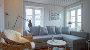 Een moderne woonkamer met een grijze bank, een rieten fauteuil, een ronde salontafel en twee vloerlampen.