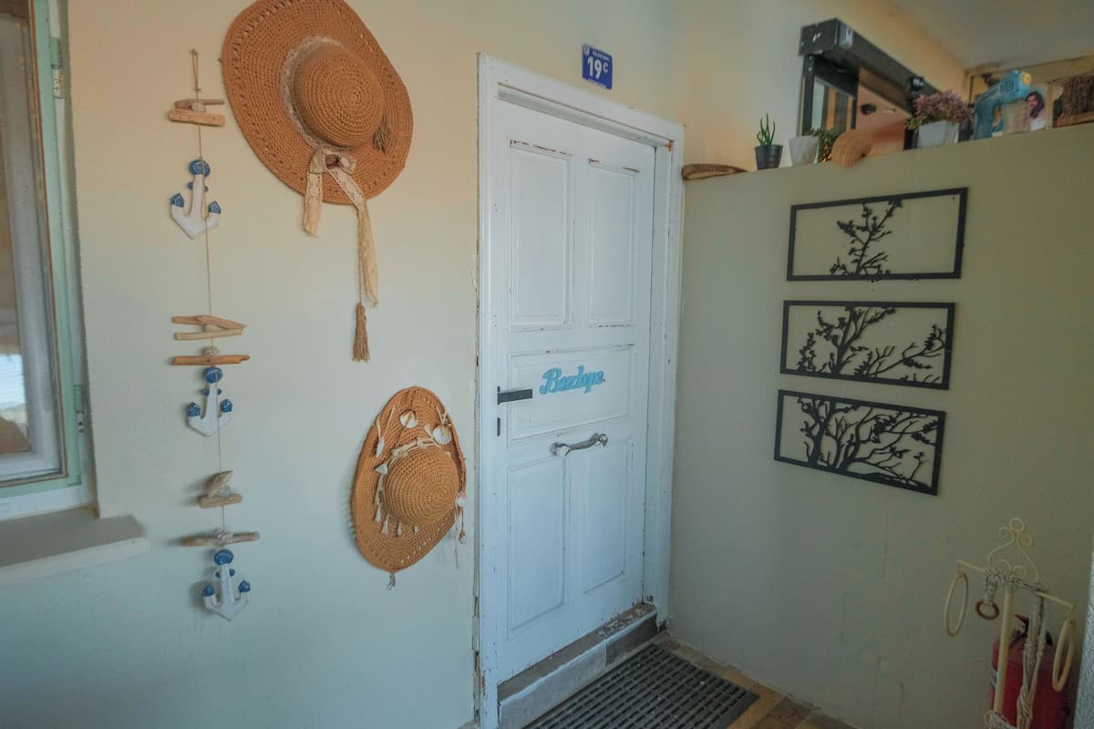 A white door with a sign above it, a wall with hanging hats and a wall-mounted plant.