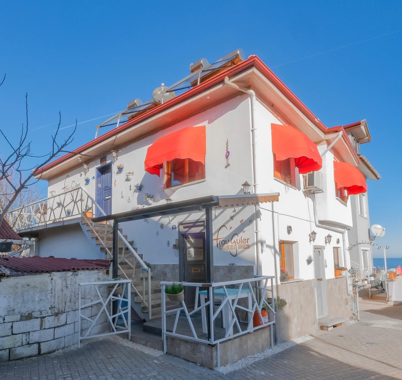 Un edificio con techo rojo, paredes blancas y varias toldillas rojas.