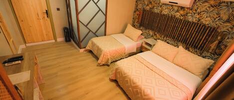 Un dormitorio con dos camas, suelo de madera, puerta corredera y aire acondicionado instalado en la pared.
