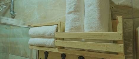 Un baño con pared de mármol, un perchero de madera con dos toallas enrolladas y un secador de pelo sobre un soporte blanco.