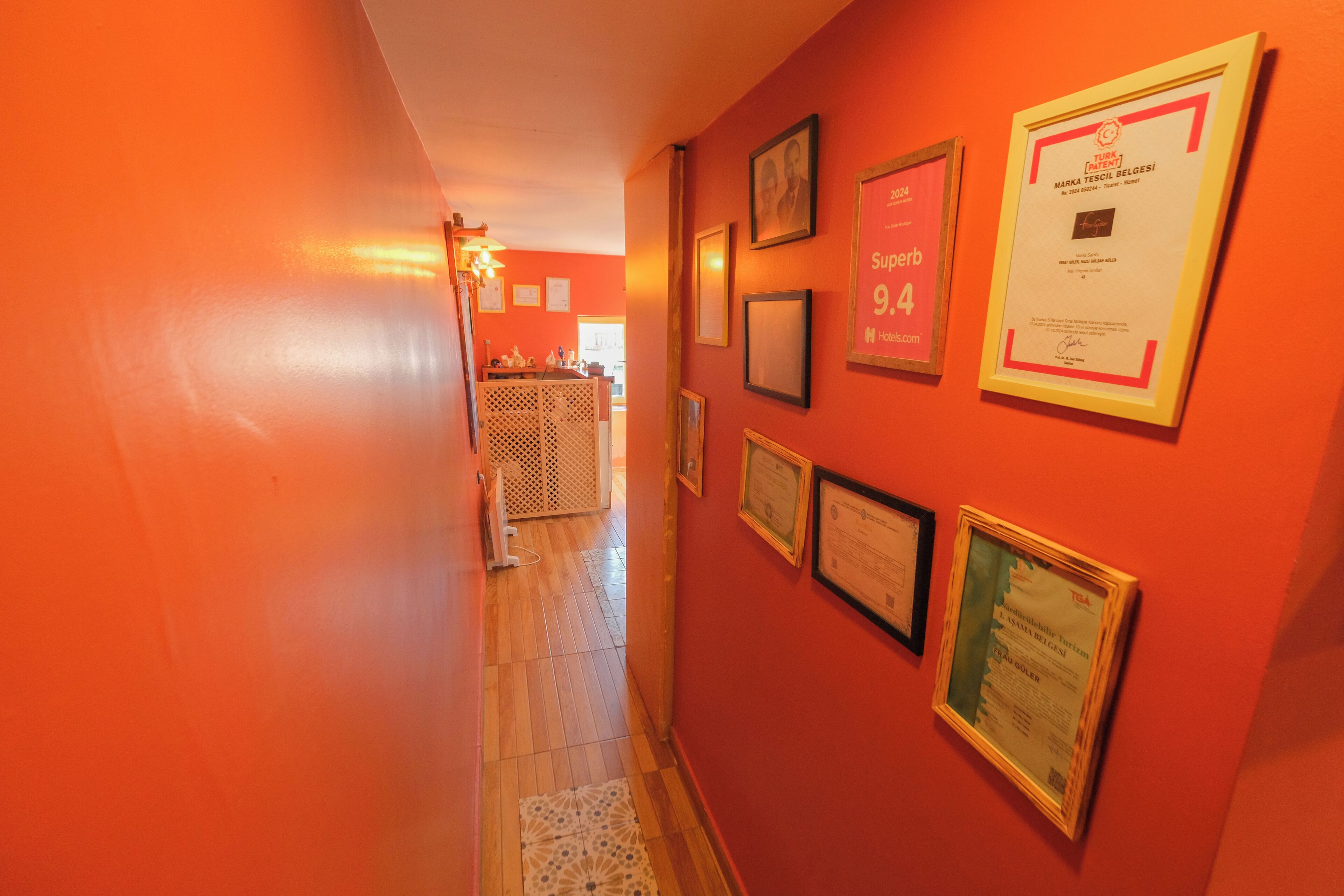 A hallway with orange walls and framed certificates on the right.