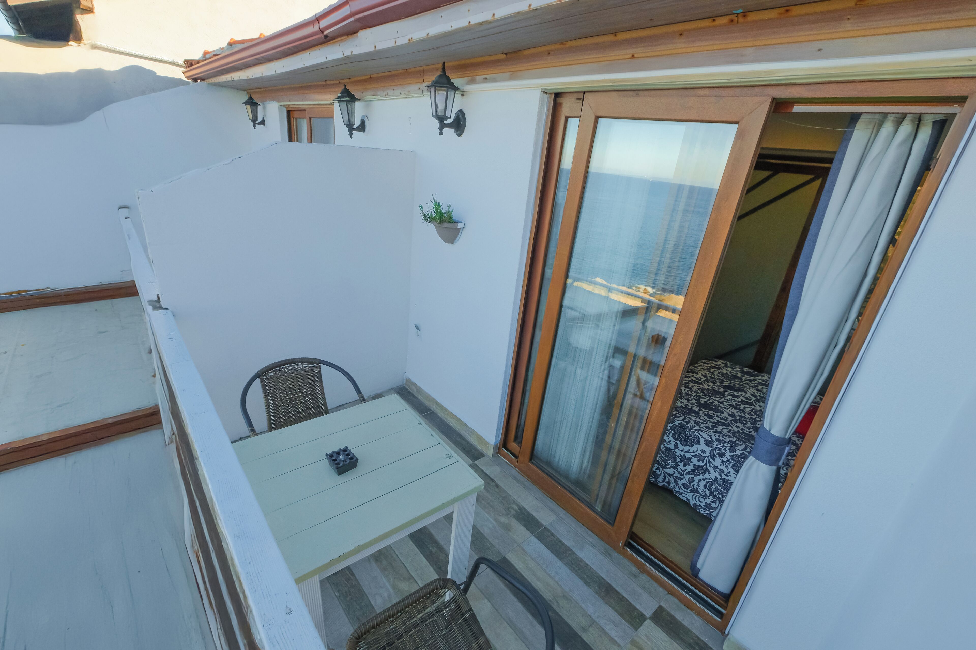A small balcony with a table and chairs, a sliding glass door, and a potted plant.