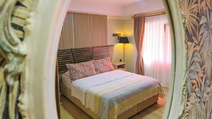 Un dormitorio con cama, mesita de noche, lámpara y ventana con cortinas.