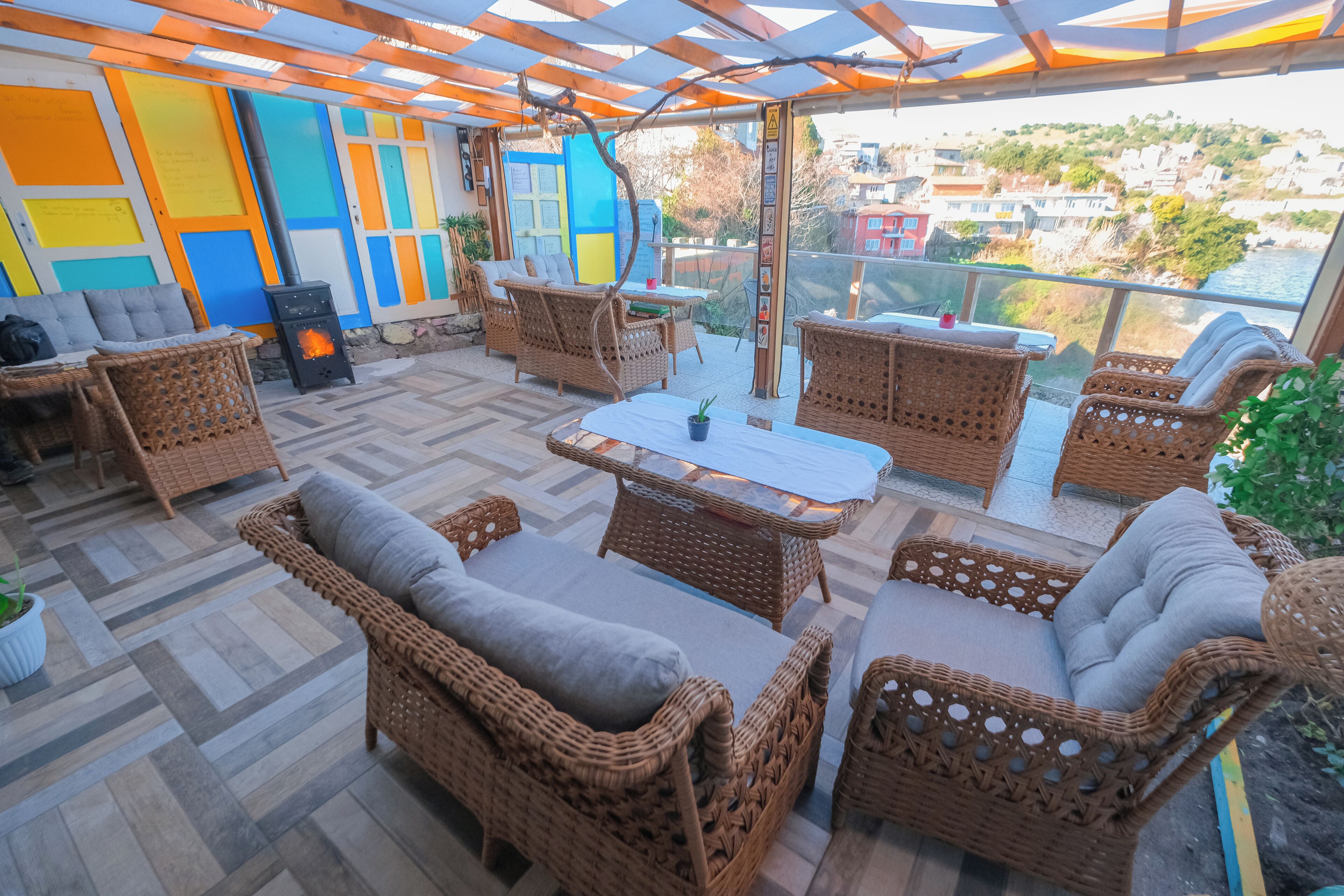 Un espacio al aire libre cubierto con mobiliario de mimbre, una mesa central y vistas a un pueblo costero.