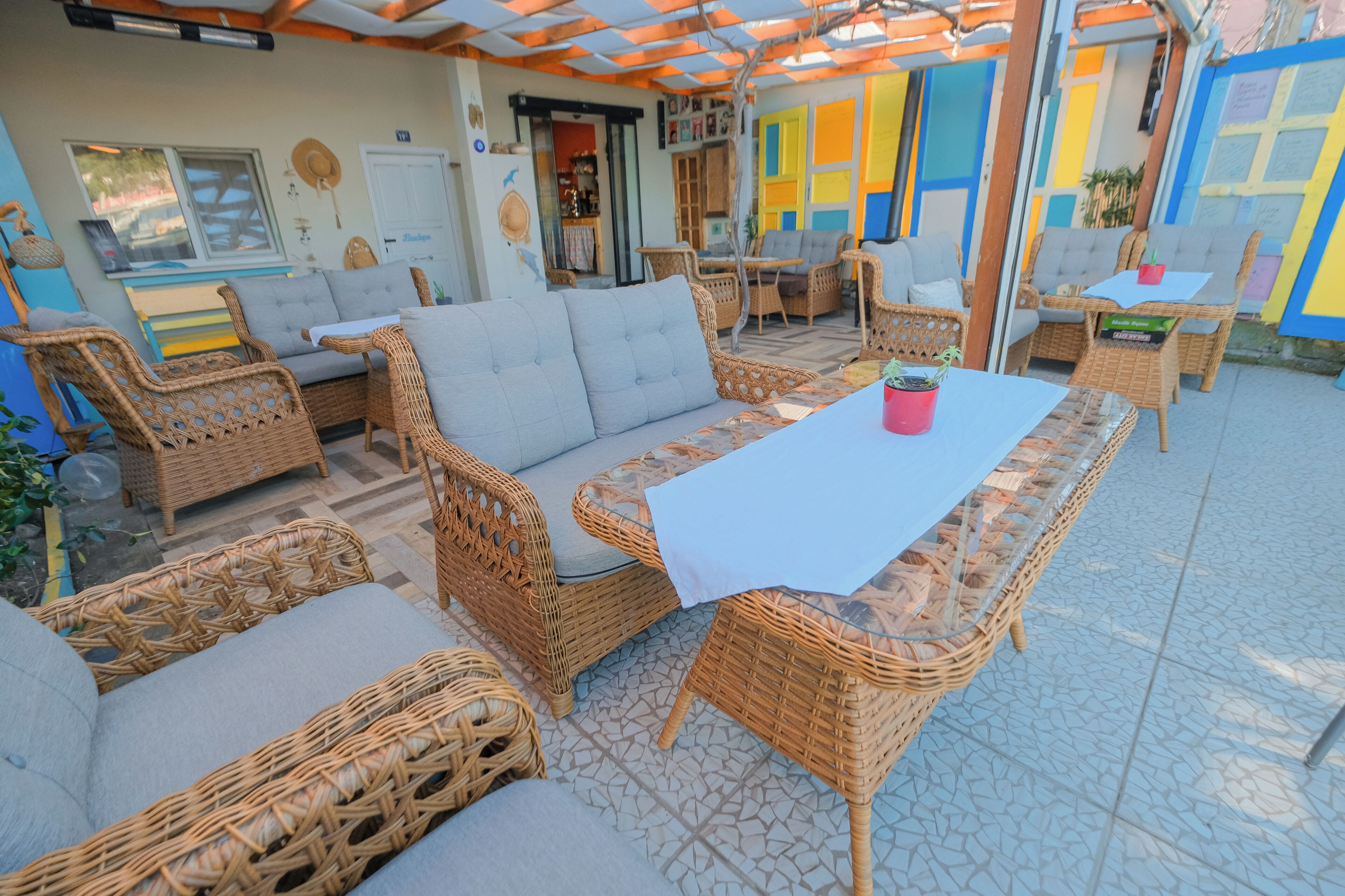 Un espacio al aire libre acogedor con mobiliario de mimbre y una mesa, rodeado de paredes coloridas y un suelo de baldosas.
