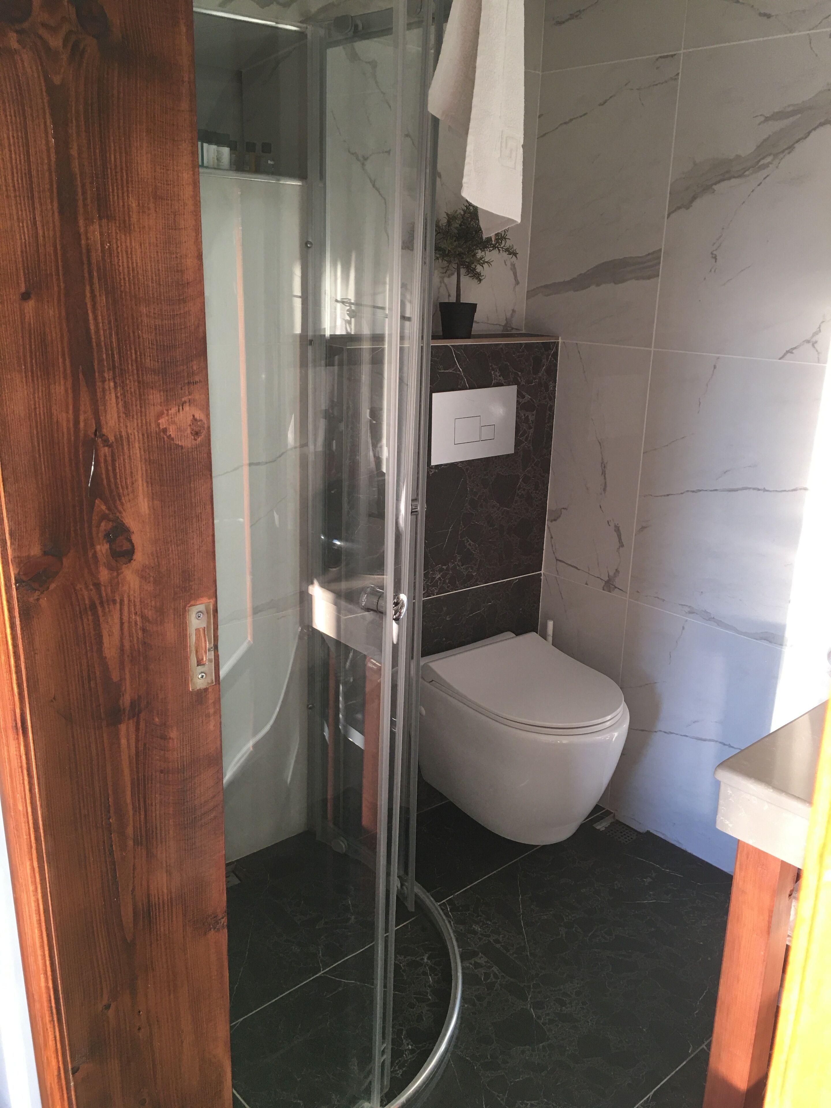 Un baño con ducha de vidrio, inodoro y pared con azulejos de mármol.