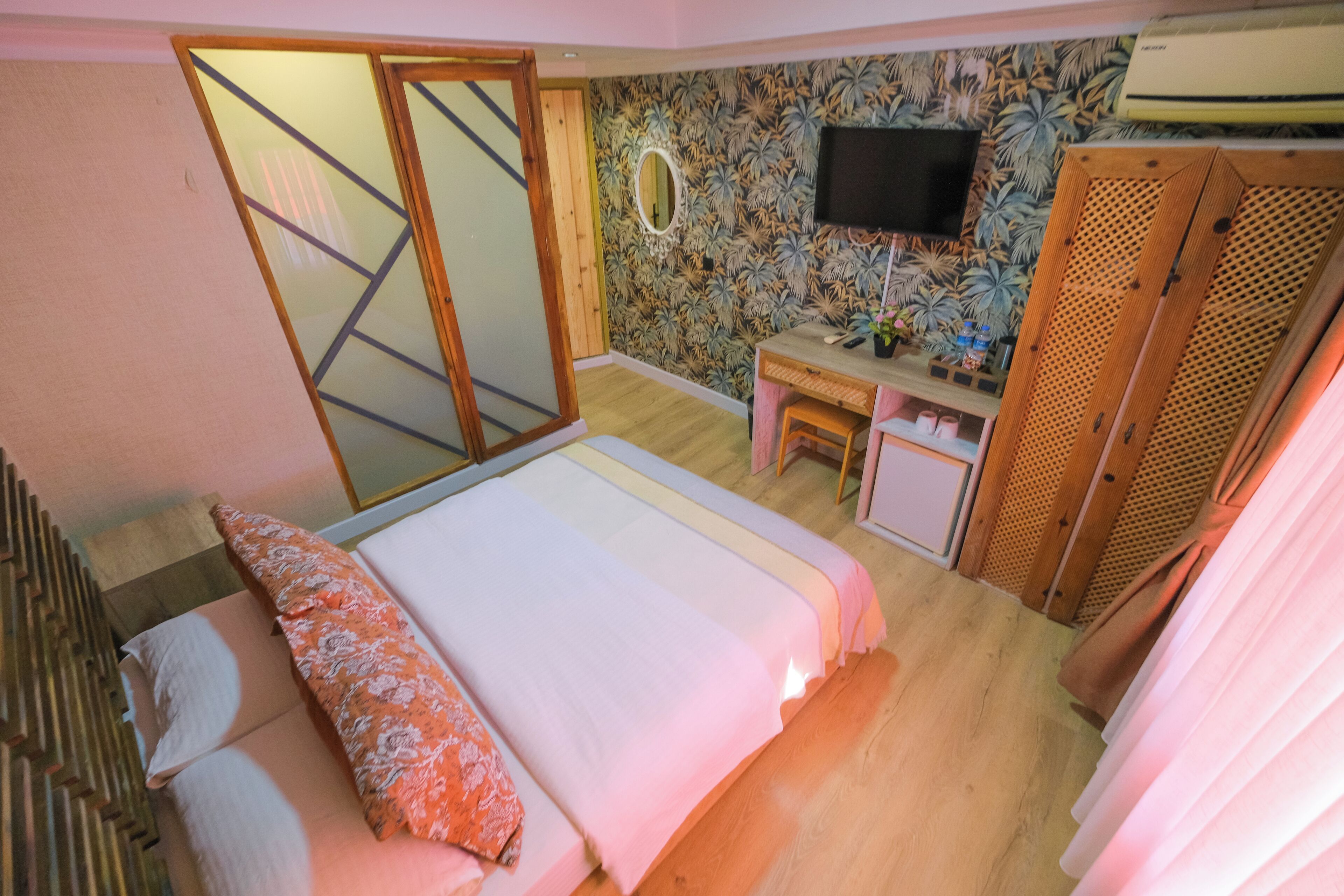 A bedroom with a bed, a desk, a mirror, and a wardrobe.