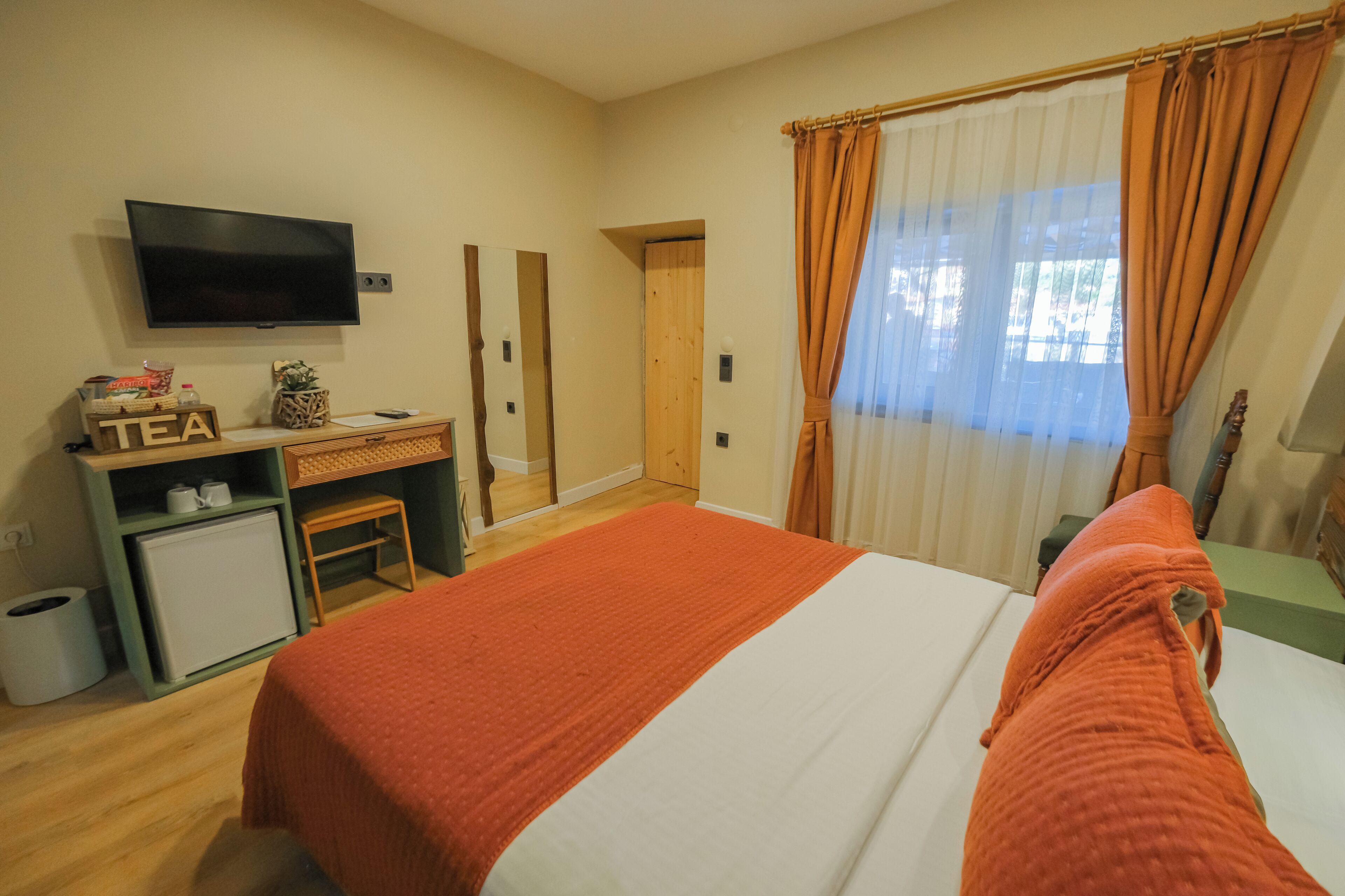 A hotel room with a bed, a desk with a computer, a television, and a window with curtains.