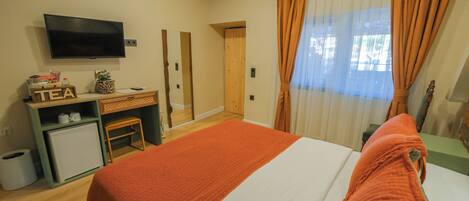 A hotel room with a bed, a desk with a computer, a television, and a window with curtains.