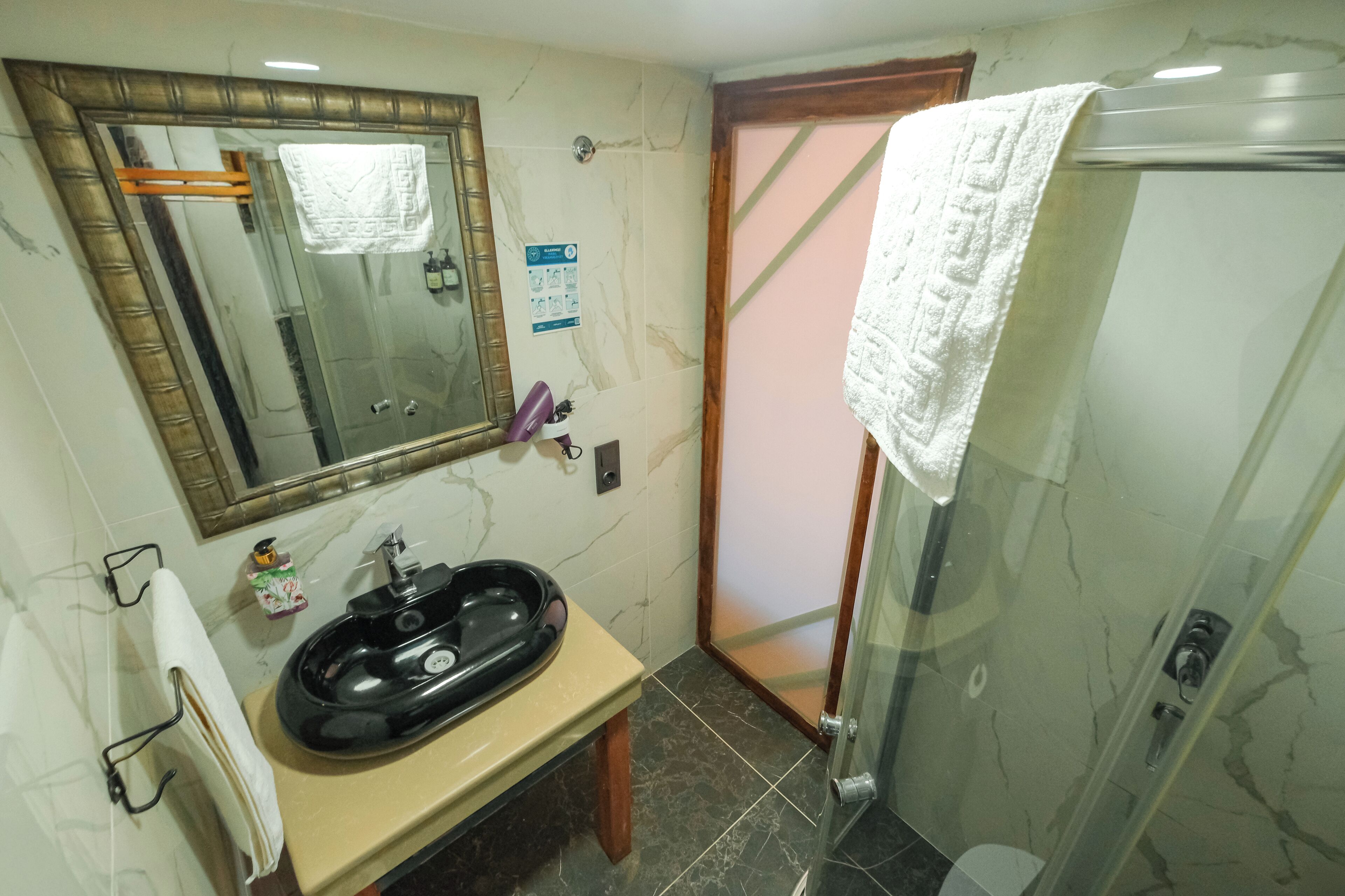 Un baño con lavamanos de mármol, un espejo, cabina de ducha de cristal y una toalla colgada en la puerta.