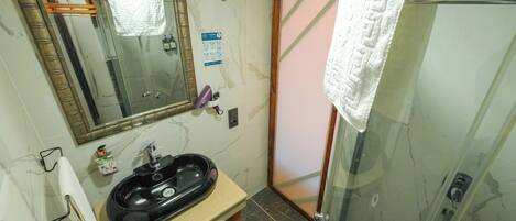 Un baño con lavamanos de mármol, un espejo, cabina de ducha de cristal y una toalla colgada en la puerta.