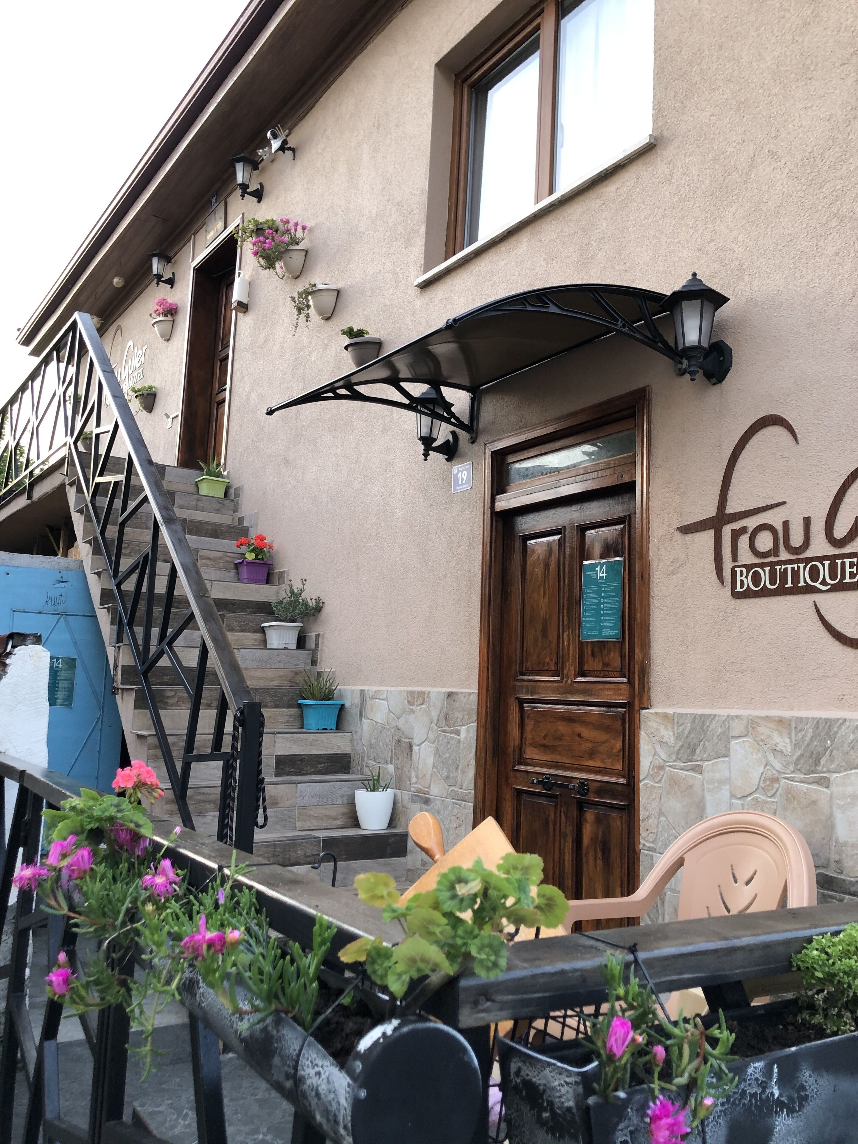 A boutique hotel entrance with a wooden door, outdoor seating, and potted plants.