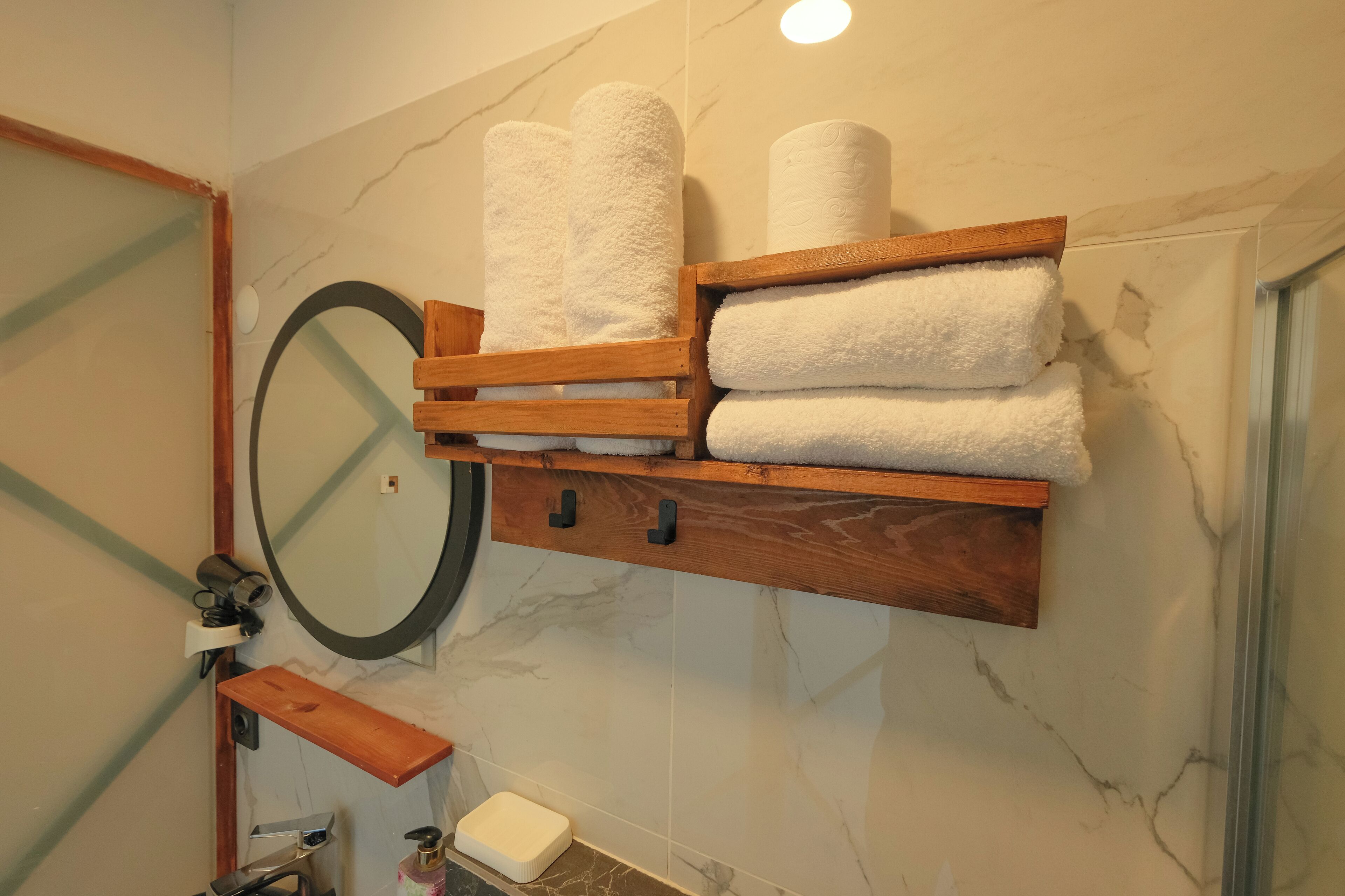 A bathroom with a wooden towel rack holding several white towels, a round mirror, and a marble wall.