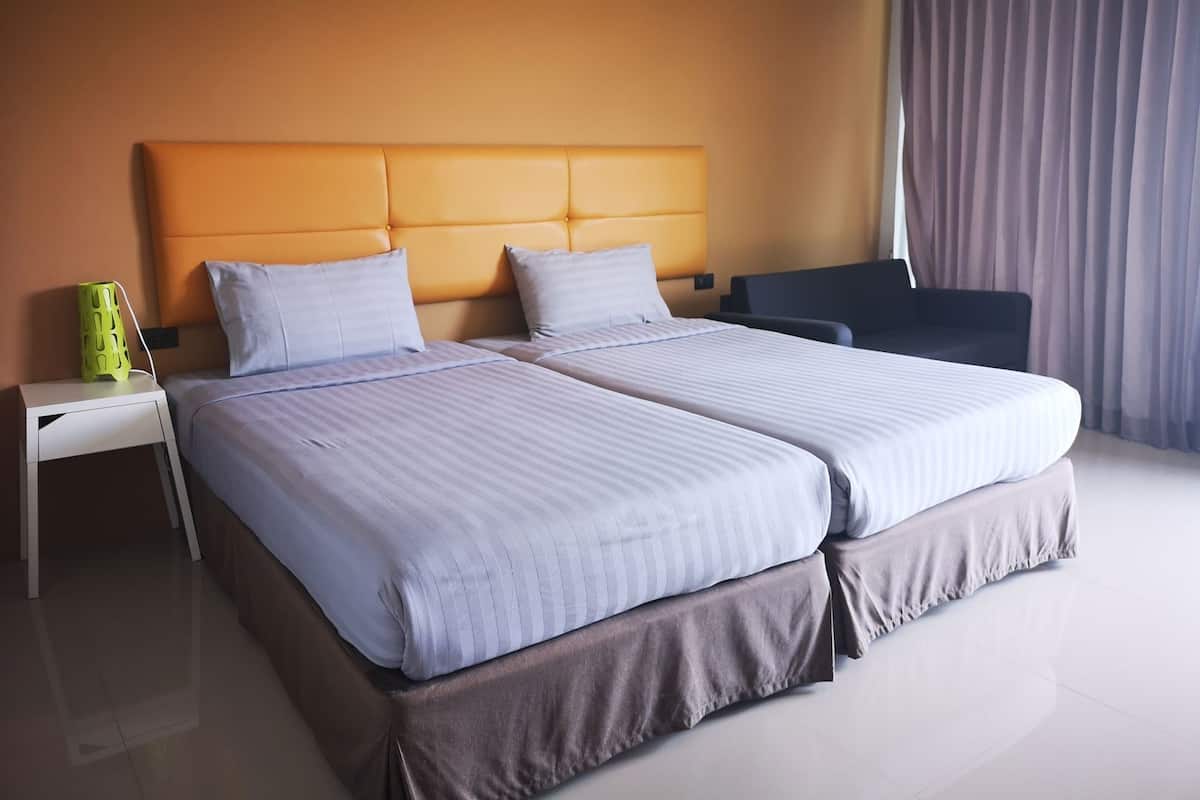 A hotel room with two beds, a nightstand, a lamp, and a chair.