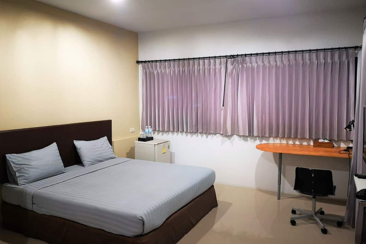 A hotel room with a bed, a desk, a chair, a small refrigerator, and a window with curtains.