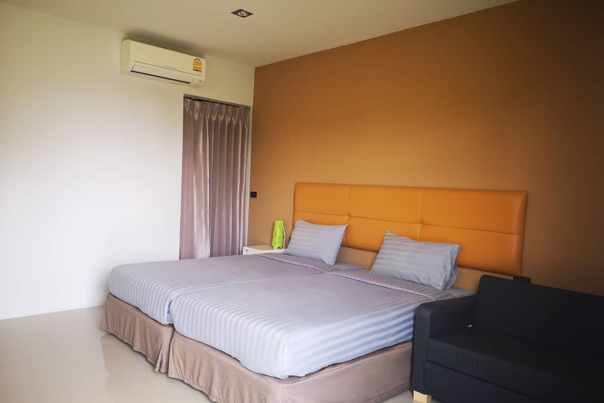 A modern hotel room with a large bed, a headboard, a nightstand, a black armchair, and an air conditioning unit.