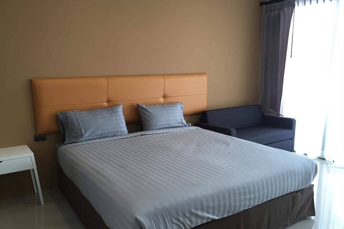 A modern hotel room with a large bed, a headboard, a bedside table, and a chair.