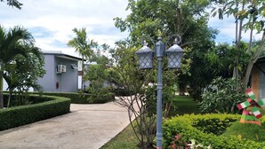 A pathway leading to a building with a modern design, surrounded by well-maintained greenery and a decorative windmill. - The Lofts Eco (Sung Noen)