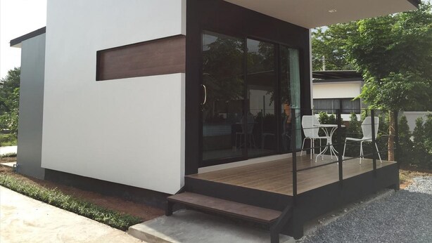 A modern, compact building with a glass entrance and a small outdoor seating area. - The Lofts Eco (Sung Noen)