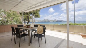 Eine Terrasse im Freien mit Tisch und Stühlen, einem Blumentopf und Blick auf Meer und Berge.
