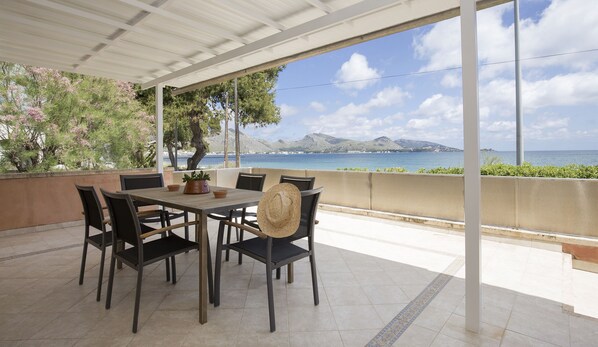 Eine Terrasse im Freien mit Tisch und Stühlen, einem Blumentopf und Blick auf Meer und Berge.