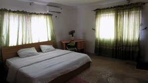 A bedroom with a bed, a desk, and a chair. There is a window with curtains and an air conditioning unit on the wall. - Royal Green Guest House (Abeokuta)