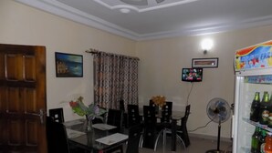 A dining area with a table, chairs, a vase with flowers, a television, and a refrigerator stocked with beverages. - Royal Green Guest House (Abeokuta)