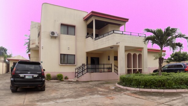 A two-story building with a balcony, a staircase, and a parking area with two cars. - Royal Green Guest House (Abeokuta)