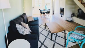 A modern living room with a sofa, coffee table, and chairs. There is a dining area with a table and chairs in the background.