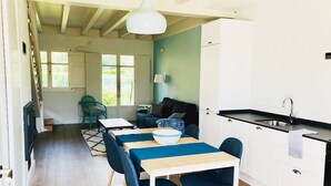 A modern kitchen with white cabinets, a black countertop, and a sink. There is a dining area with a table and chairs, and a sofa in the background.