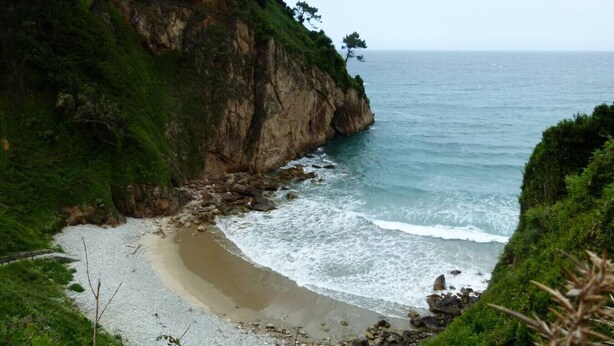 A coastal landscape with a sandy beach, rocky cliffs, and a view of the sea.