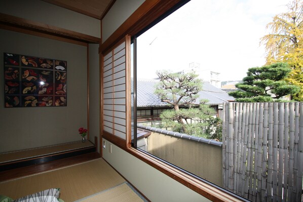 A traditional Japanese room with tatami flooring, a shoji screen, and a view of a bamboo fence and trees.