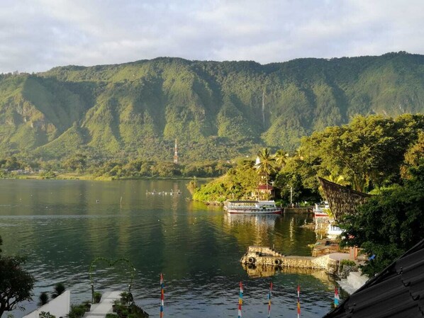 Un lago con un bote amarrado a la derecha, rodeado de colinas verdes y un cielo despejado.