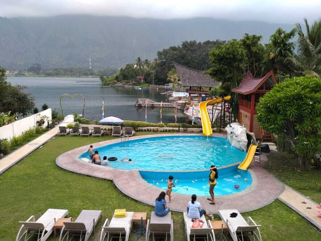 Une piscine avec un toboggan, entourée de chaises longues et offrant une vue sur un lac et des montagnes.