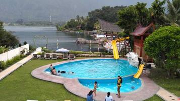 A swimming pool with a slide, surrounded by lounge chairs and a view of a lake and mountains.