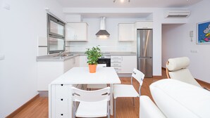 A modern kitchen with white cabinets, a stainless steel refrigerator, and a dining area with white chairs and a table. - Nice frontline apartment in Playa de Arinaga (Arinaga)