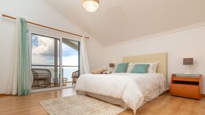 Quarto com uma cama grande, mesa de cabeceira de madeira, abajur, janela com cortinas e vista para o exterior.