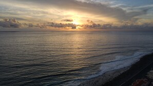 Vista do pôr do sol na costa, com praia e uma estrada ao longo da orla.