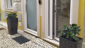A hotel entrance with a tiled pavement, a door with a frosted glass panel, and a potted plant beside it. - Ferhouse Dreams- Farilhões (Nazaré)