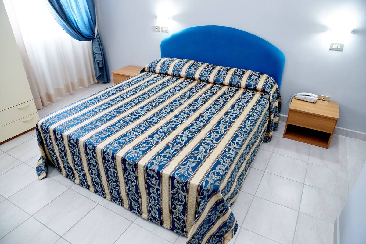 A neatly made bed with a blue headboard, a bedside table with a phone, and a nightstand with a lamp.