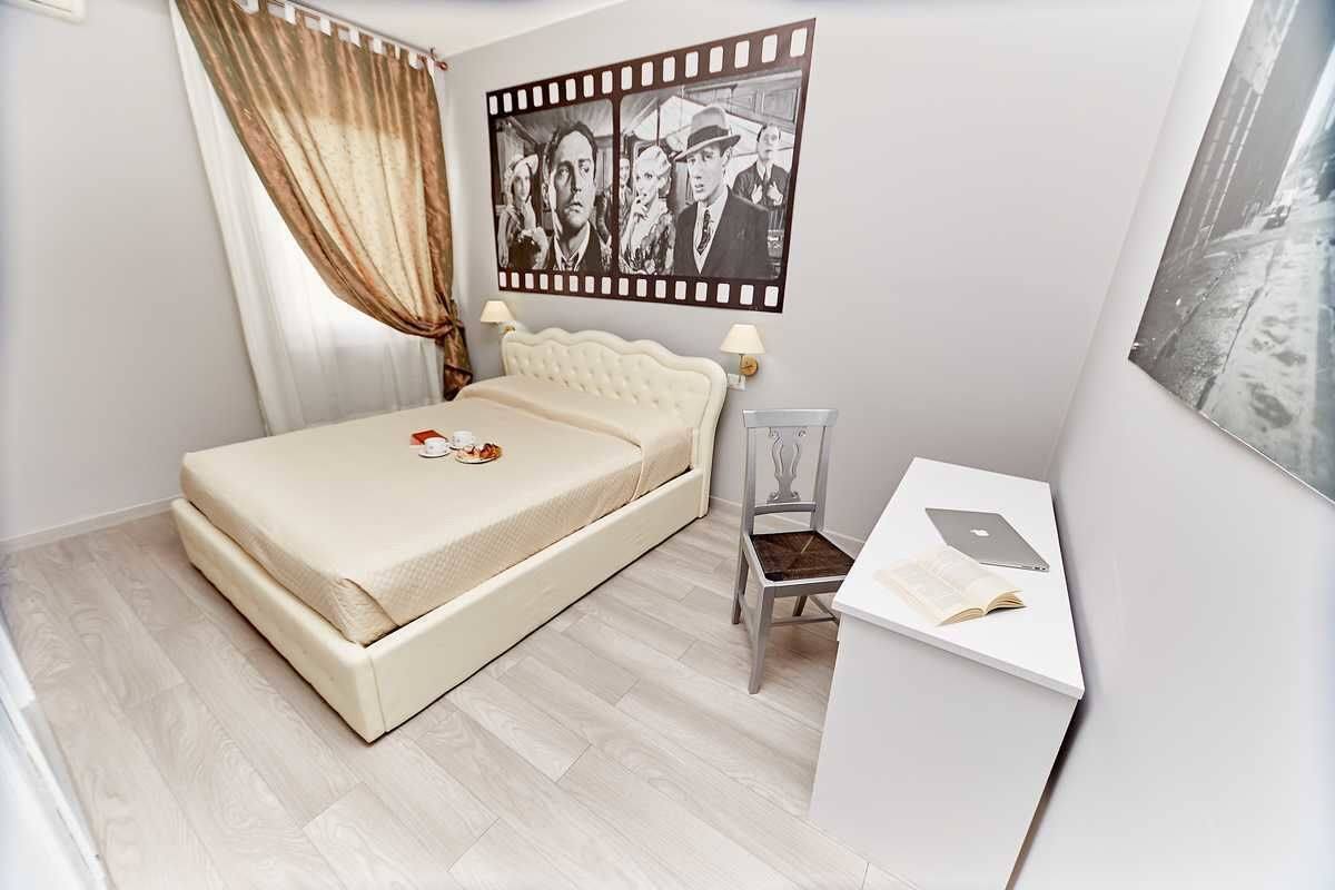 A bedroom with a bed, a desk with a laptop, and a filmstrip artwork on the wall.