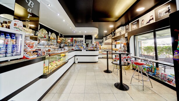 Un área de bar moderna con mostrador, vitrina refrigerada y asientos.