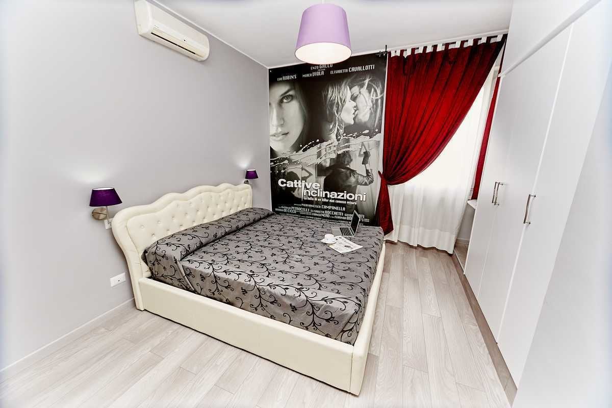 A bedroom with a white bed, a poster on the wall, a red curtain, and a ceiling light.