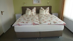 Ein Doppelbett mit floralem Bettzeug, zwei Nachttische, ein Tischchen, eine Tür und ein gerahmtes Bild an der Wand.