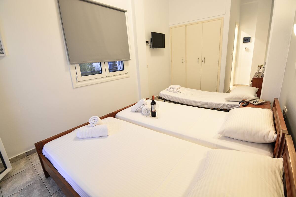 Hotelkamer met twee enkele bedden, een aan de muur bevestigde televisie, een kledingkast en een raam met gordijn.