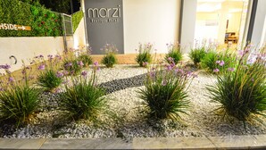Un jardin aménagé avec des fleurs violettes et une enseigne indiquant « Marzi Boutique Hotel ».