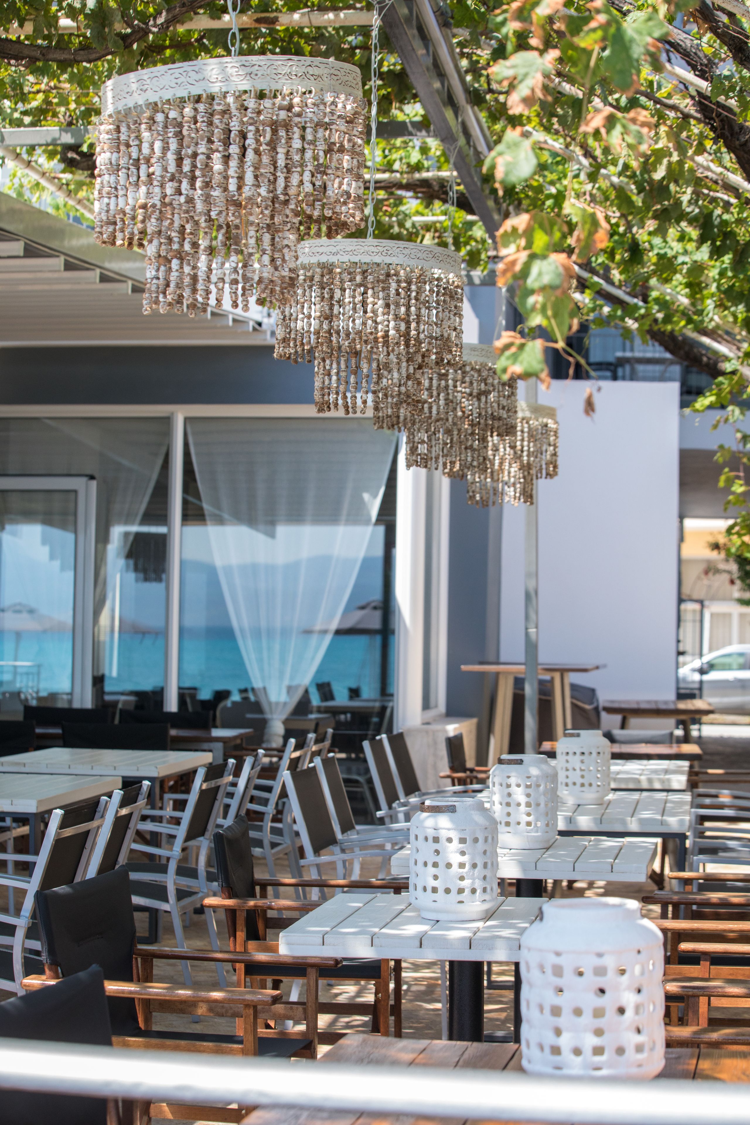 An outdoor dining area with wooden tables and chairs, white lanterns, and a decorative hanging light fixture.