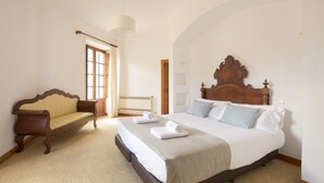 Een slaapkamer met een groot bed, een houten bankje en een raam met gordijnen.